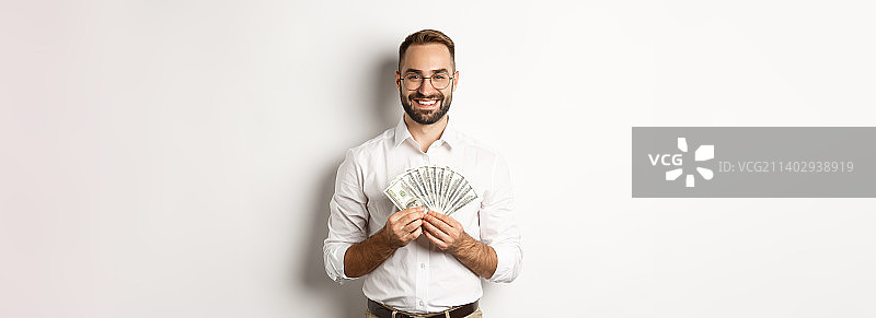 微笑的英俊男子拿着钱，显示美元，站在图片素材
