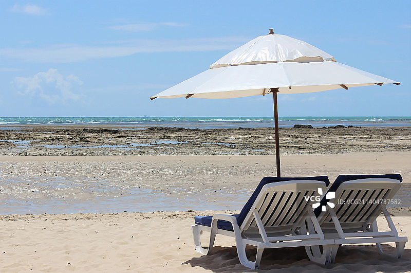 海滩景观与两个太阳躺椅和遮阳伞上的沙子和海洋和天空的背景，巴西图片素材
