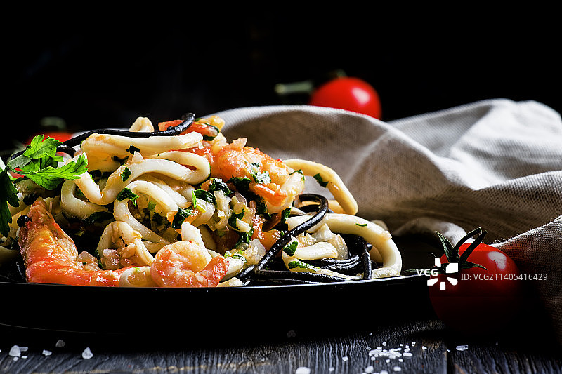 黑色的意大利面配海鲜和番茄酱在盘子里，黑色的背面图片素材