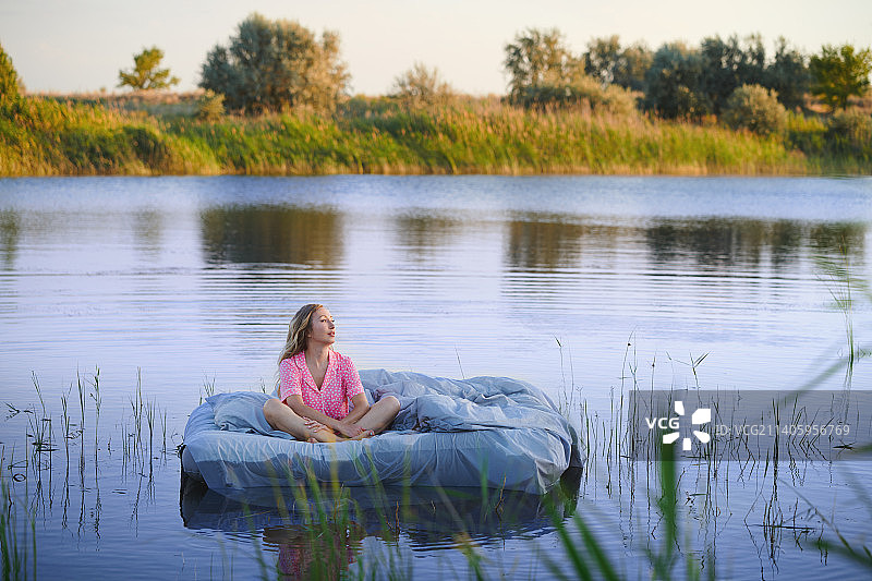 性感的金发女人在粉红色圆点睡衣坐在床上的湖中央在早上。很适合做书的封面。超现实主义的概念图片素材