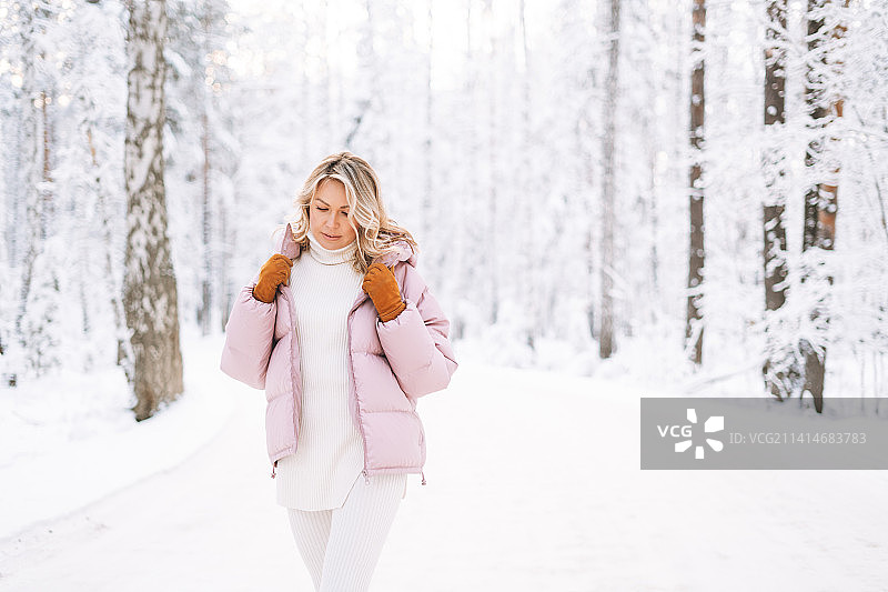 俄罗斯斯维尔德洛夫斯克州叶卡捷琳堡，年轻的金发女子穿着冬装走在白雪覆盖的冬季森林里图片素材