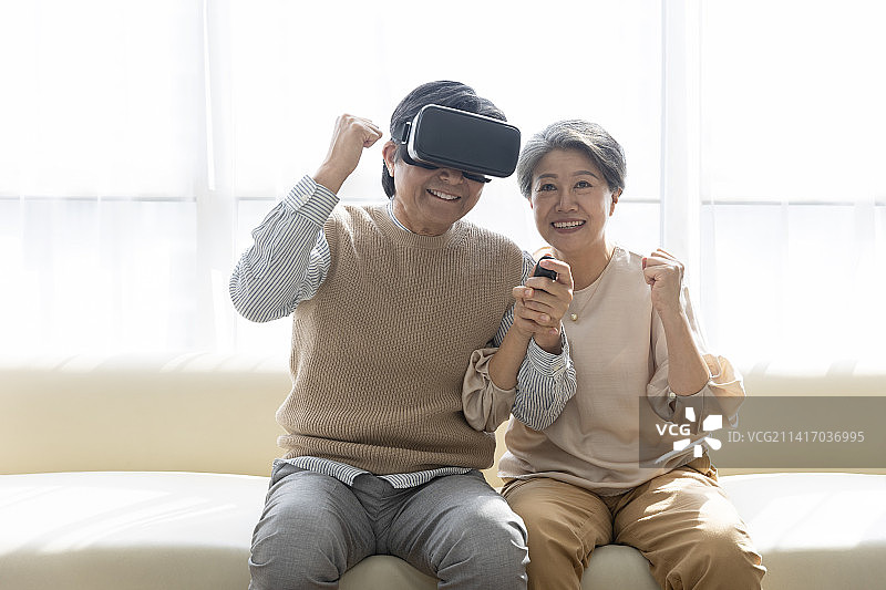 老年夫妇在客厅玩虚拟现实模拟器，欢呼庆祝胜利图片素材