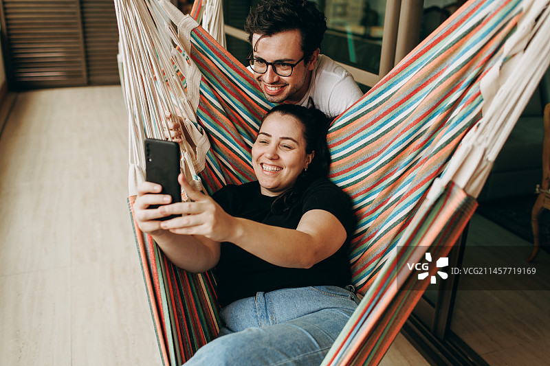 巴西米纳斯吉拉斯州贝洛奥里藏特，一对躺在吊床上玩手机的夫妇的高角度照片图片素材