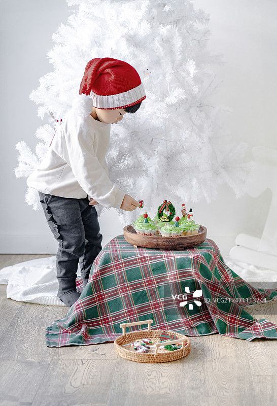 可爱男孩在白色圣诞树处装饰圣诞蛋糕图片素材