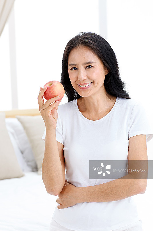 中年女人拿着苹果在卧室图片素材