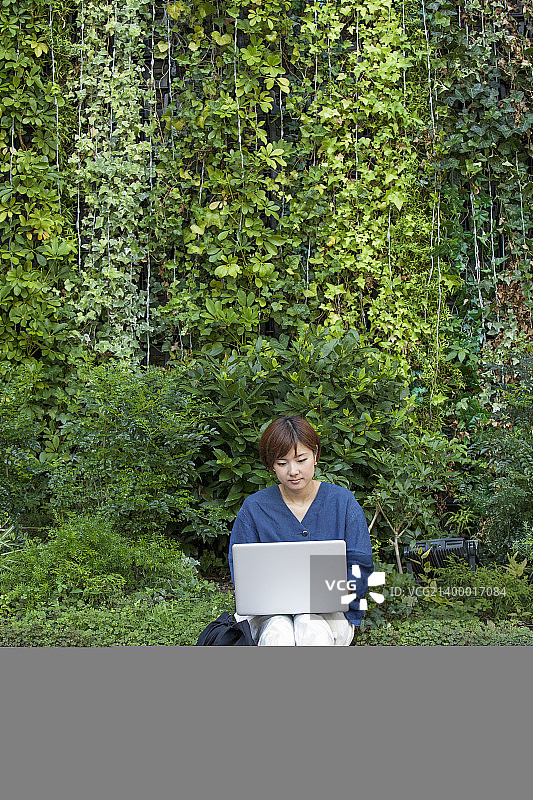 一个拿着笔记本电脑坐在户外的女人。图片素材