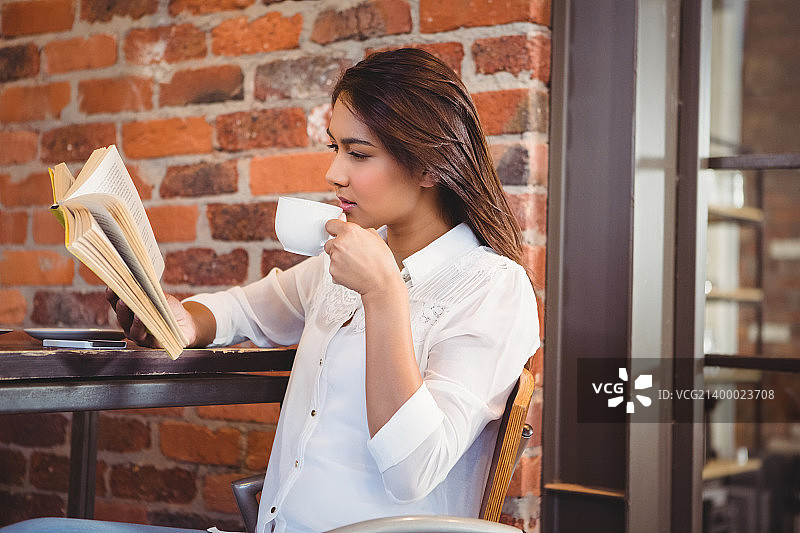 美丽的女商人在咖啡店外面喝咖啡看书图片素材