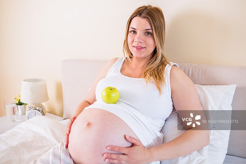 孕妇躺在床上，肚子里有苹果在家图片素材