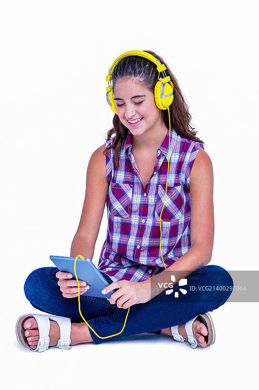 一个漂亮的黑发姑娘正在用白色背景的平板电脑听音乐图片素材