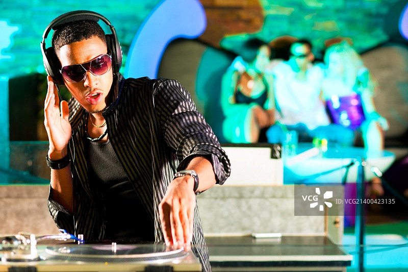 黑人DJ在一家俱乐部的唱机转盘旁，背景中人群在欢呼图片素材