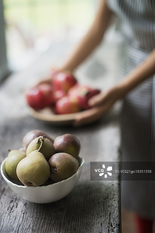 在厨房里准备有机新鲜农产品的人。一盘红苹果。碗梨。图片素材