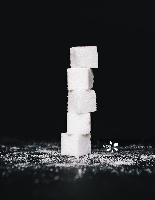 一堆方糖，一个在另一个上平衡，在黑色的背景图片素材