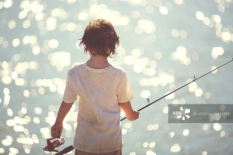 男孩(6-7)拿着鱼竿的后视图图片素材
