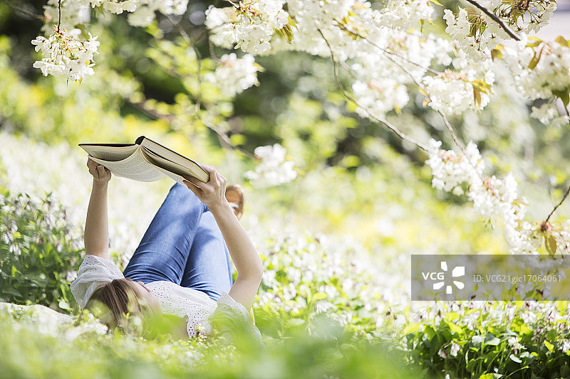 一个女人在开着白花的树下的草地上看书图片素材