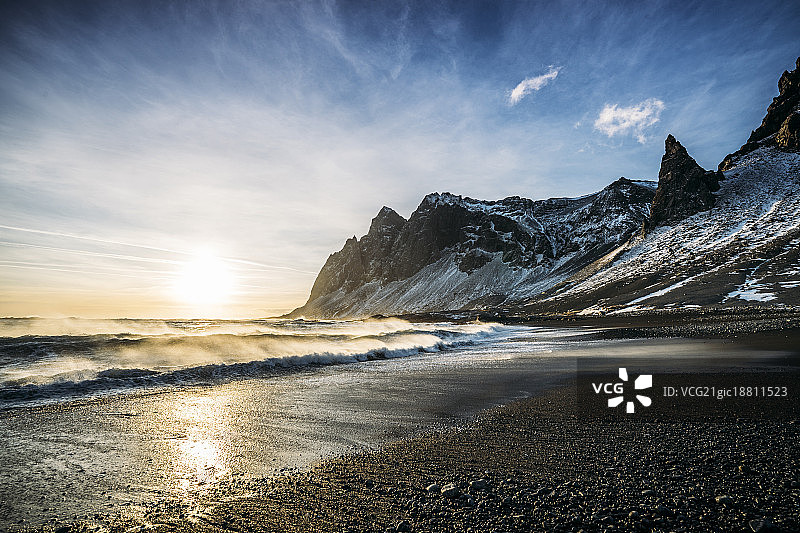 太阳落在宁静的海滩和雪山，冰岛图片素材