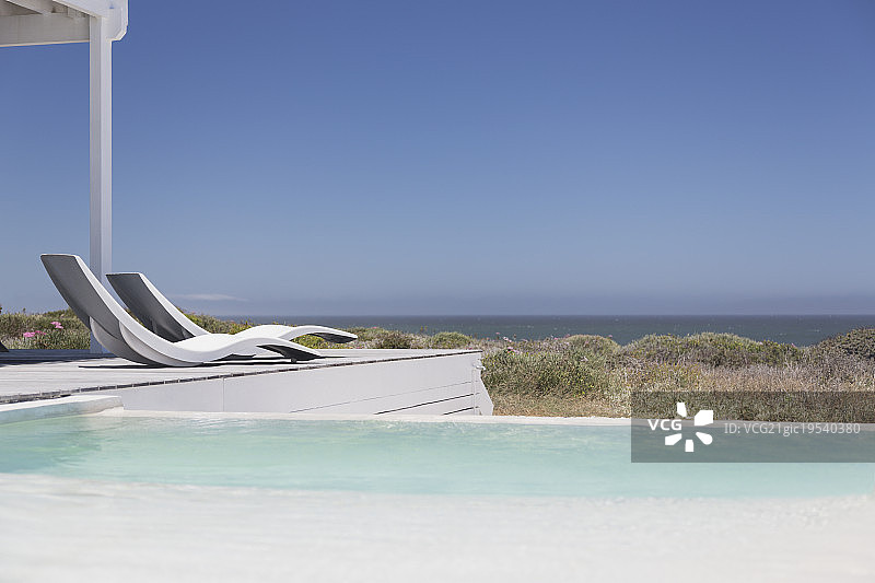 游泳池和现代躺椅俯瞰阳光明媚的蓝天下的海景图片素材