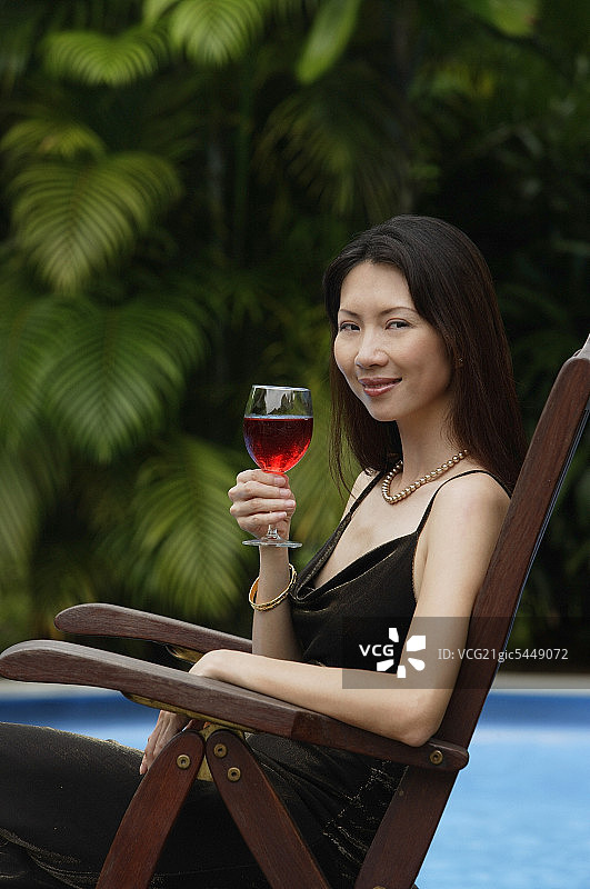 女人坐在游泳池旁，拿着一杯酒，画像图片素材
