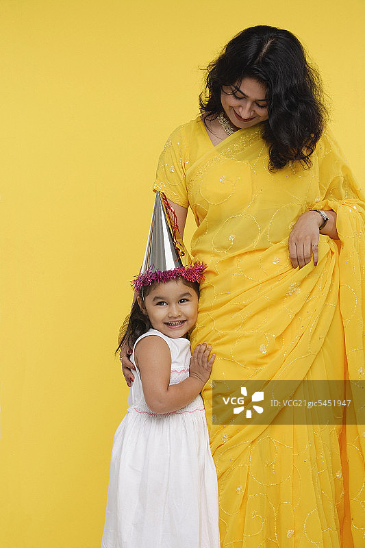 年轻的女孩穿着白色的裙子和派对帽，站在她的母亲旁边图片素材