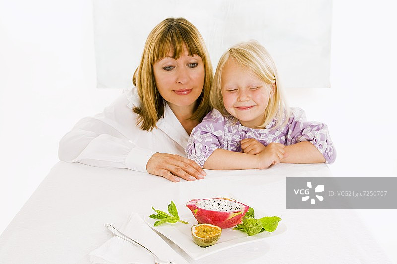 母亲和女儿坐在桌前，桌上放着一盘水果图片素材