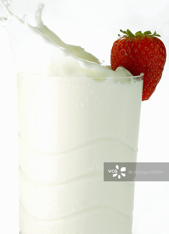 牛奶从装有草莓的玻璃杯里溅了出来图片素材