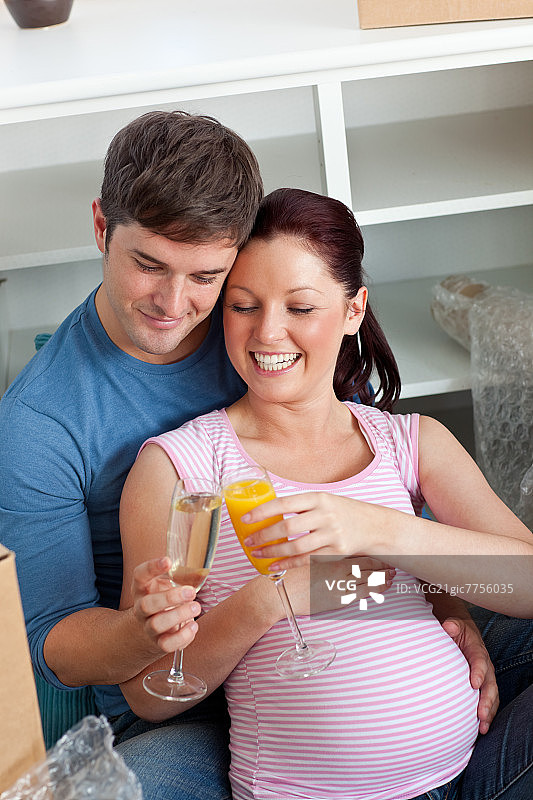 一对期待孩子出生的快乐夫妇坐在家里的地板上喝酒图片素材