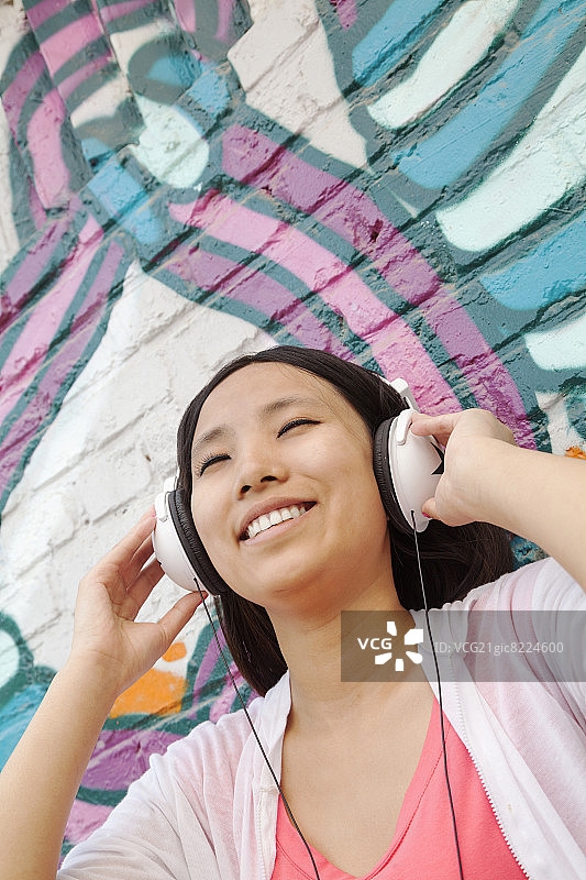 年轻的女人微笑着拿着她的耳机，享受着音乐在墙上涂鸦图片素材