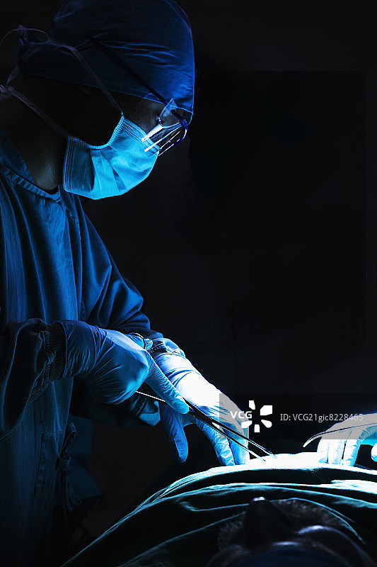 医生向下看，工作，并拿着手术设备，病人躺在手术台上图片素材
