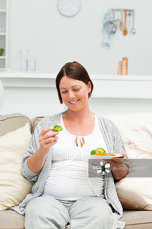 坐在沙发上吃蔬菜的孕妇图片素材