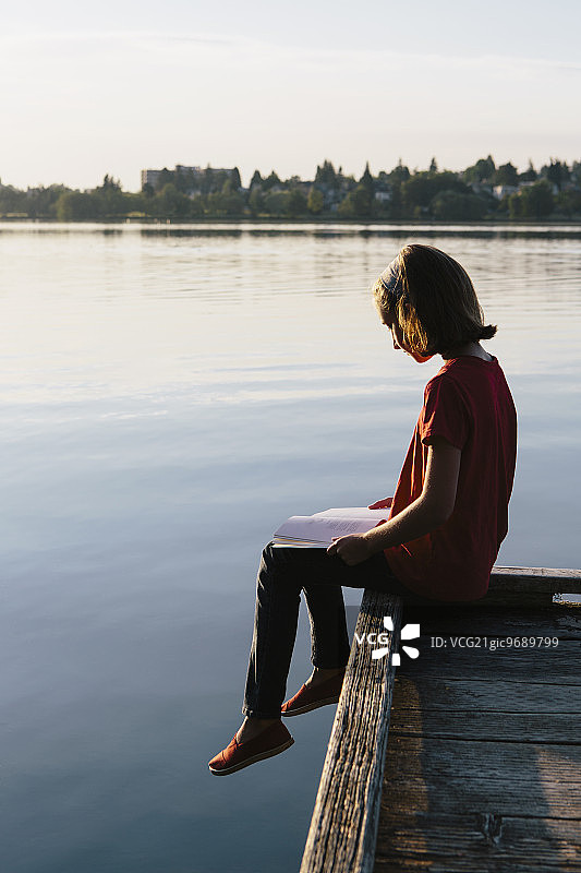 一个年轻的女孩坐在码头上，在读一本书。图片素材