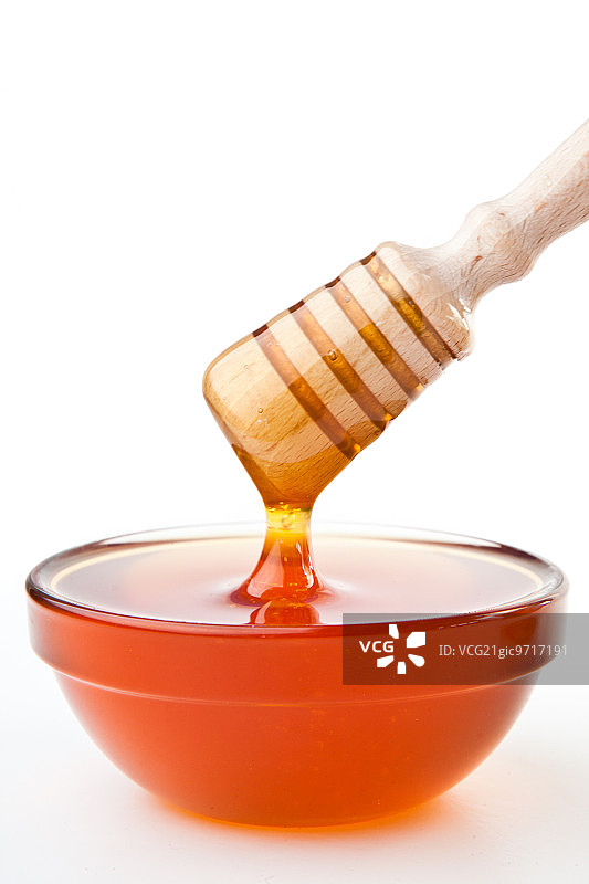 在白色背景下，蜂蜜勺放在蜂蜜碗上图片素材