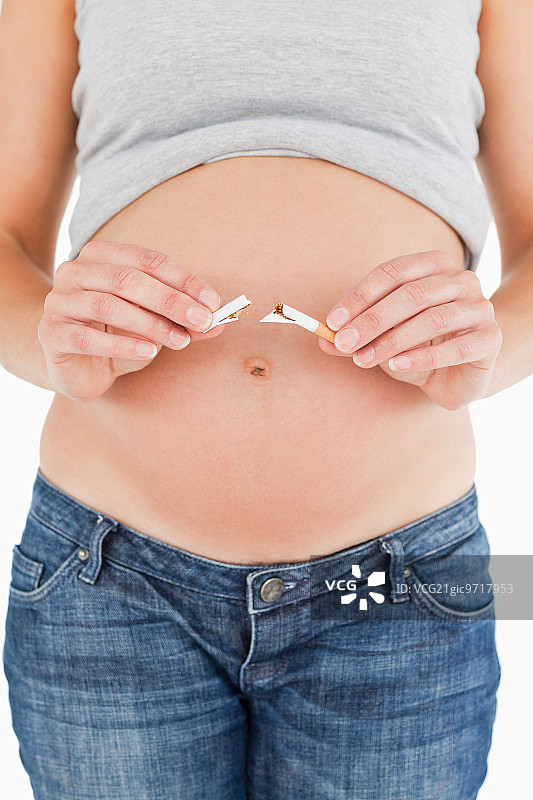 一名孕妇拿着一支断了的香烟，站在白色背景下图片素材