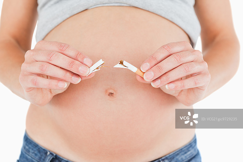 一名年轻孕妇手持一根断了的香烟，站在白色背景下图片素材