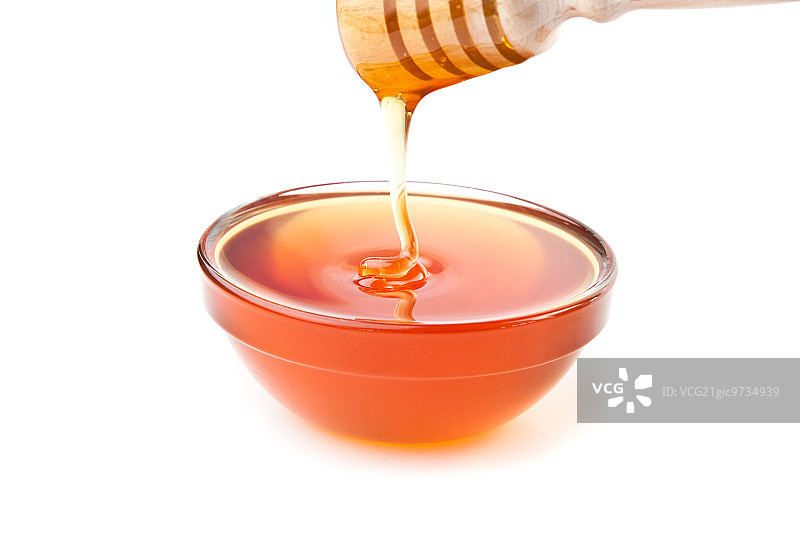 蜂蜜在白色的背景下滴落在蜂蜜碗里图片素材