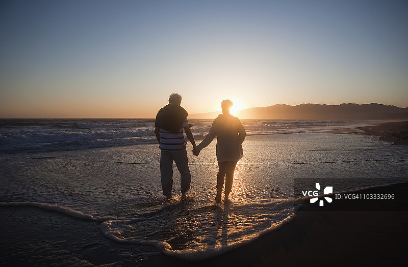 日落时分，一对老年夫妇在海滩上手拉手图片素材