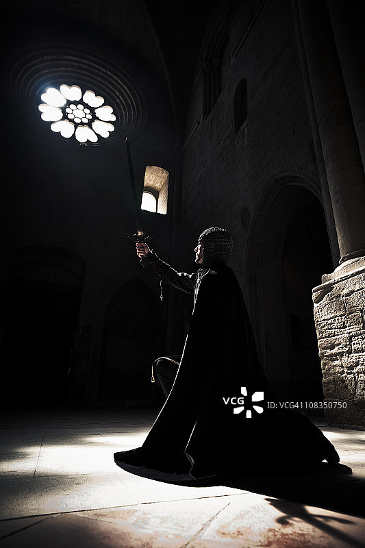 誓言跪骑士举起剑，对着大教堂的光祈祷。图片素材