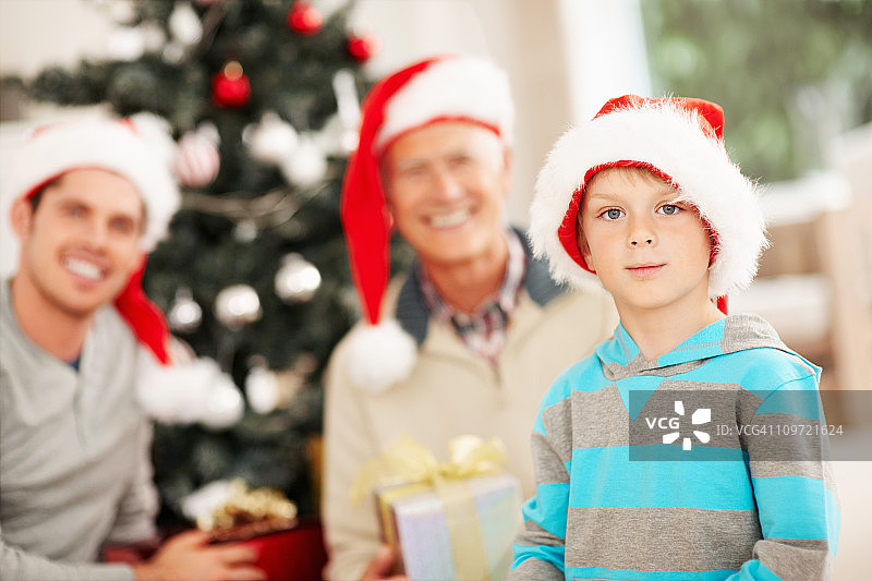 小男孩戴着圣诞老人的帽子，背景是他的家人图片素材