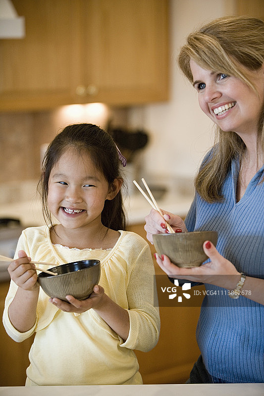 母亲和女儿在厨房拿着碗米饭和筷子的肖像图片素材
