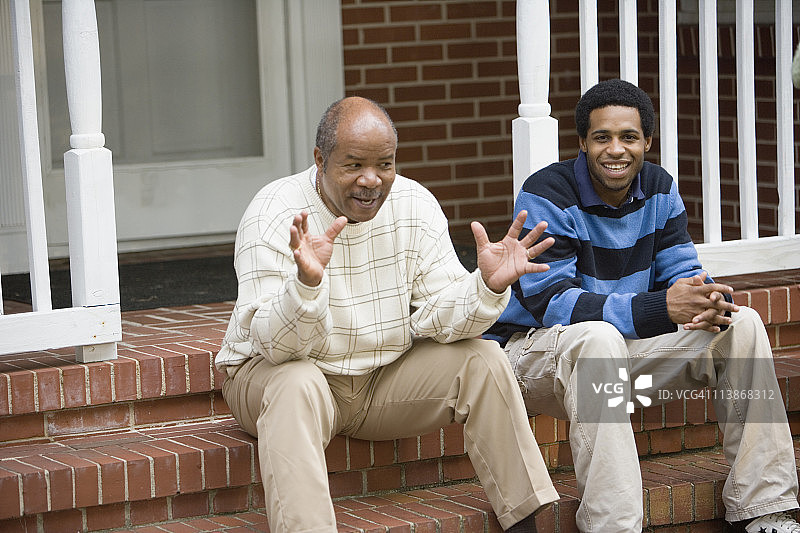 成熟的男人和成年的儿子坐在屋前的门廊上图片素材