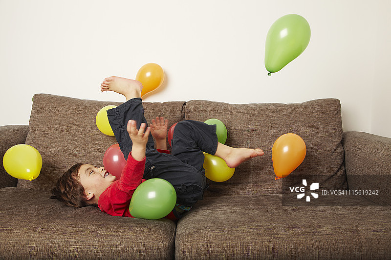 小男孩躺在沙发上踢气球图片素材