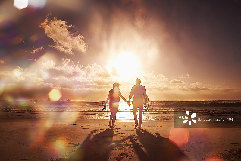 一对情侣在海滩上散步，夕阳下的剪影图片素材