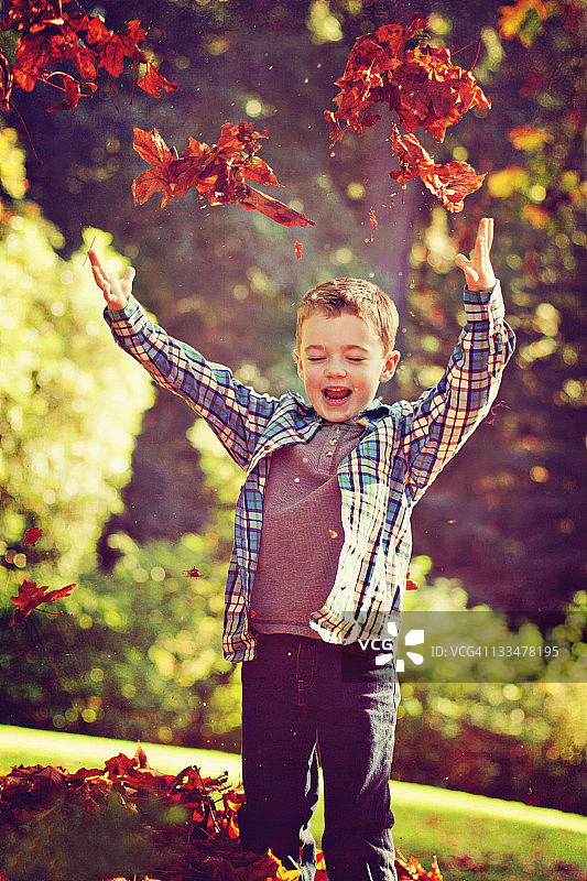 快乐的男孩把树叶抛向空中图片素材