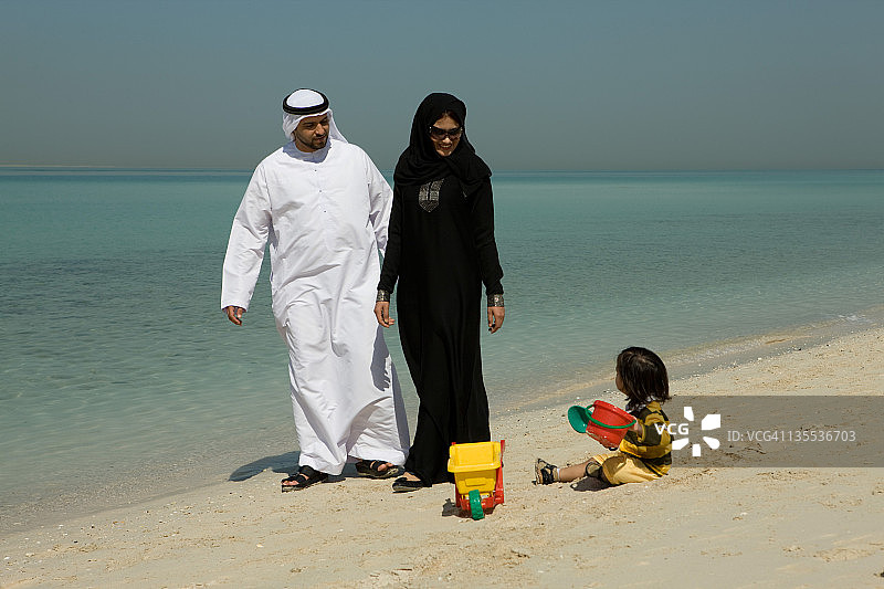 一对阿拉伯夫妇看着他们的儿子在海滩上玩耍图片素材