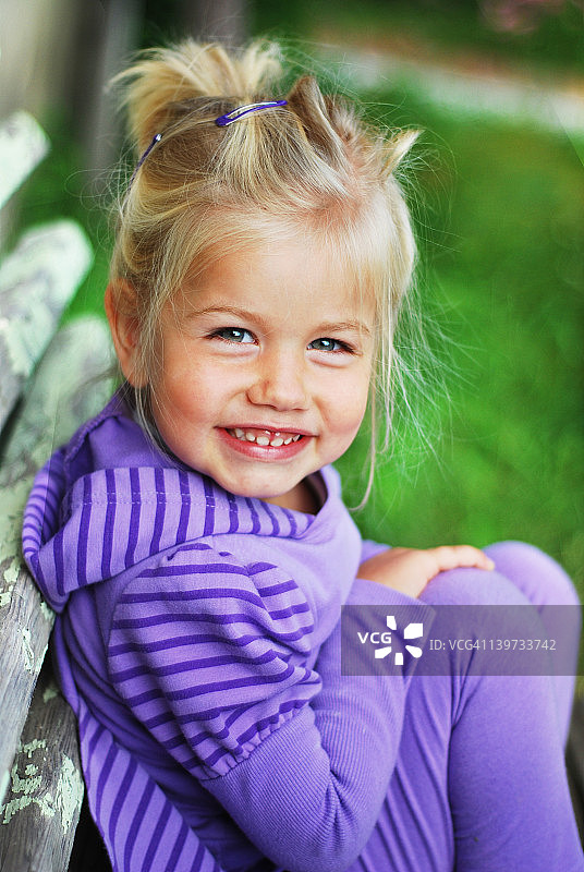 微笑的金发女孩坐在后院的长凳上图片素材