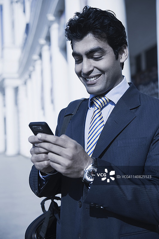 特写的一个商人短信在手机上和微笑，古尔加翁，哈里亚纳，印度图片素材