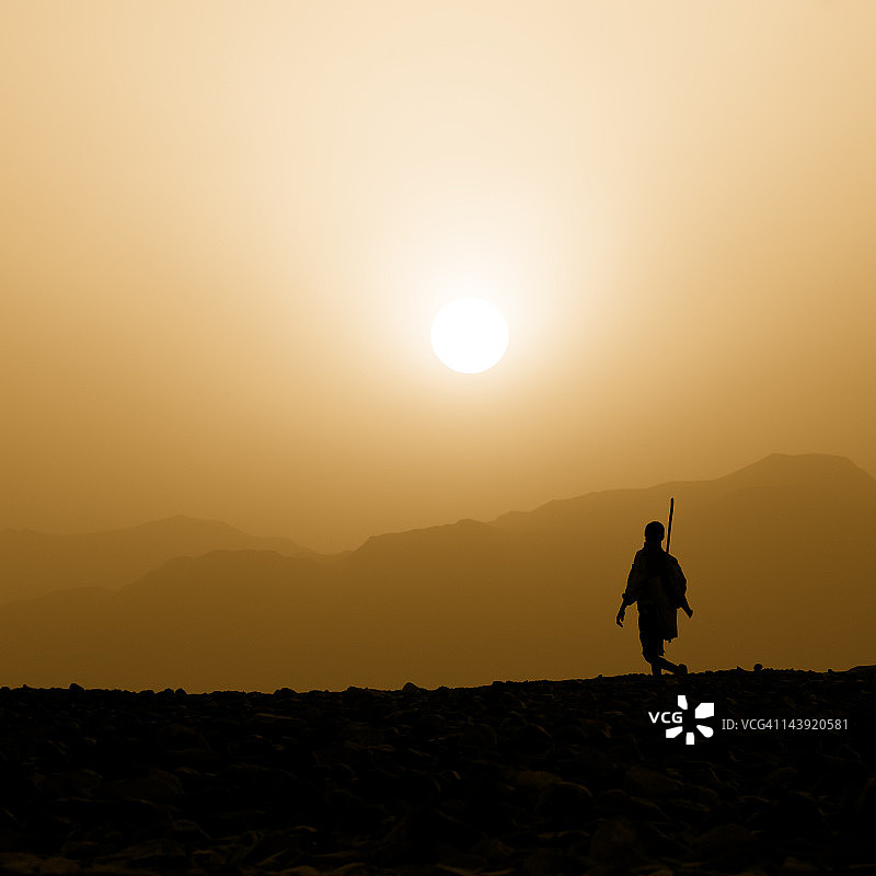达纳基尔沙漠，一名阿法尔牧人在夕阳下行走图片素材