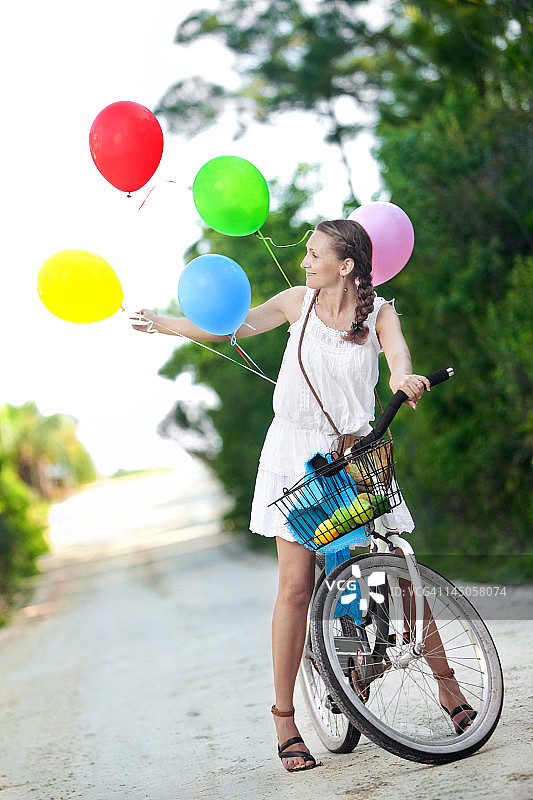 一名年轻女子停下来，拿着绑在自行车上的气球。图片素材
