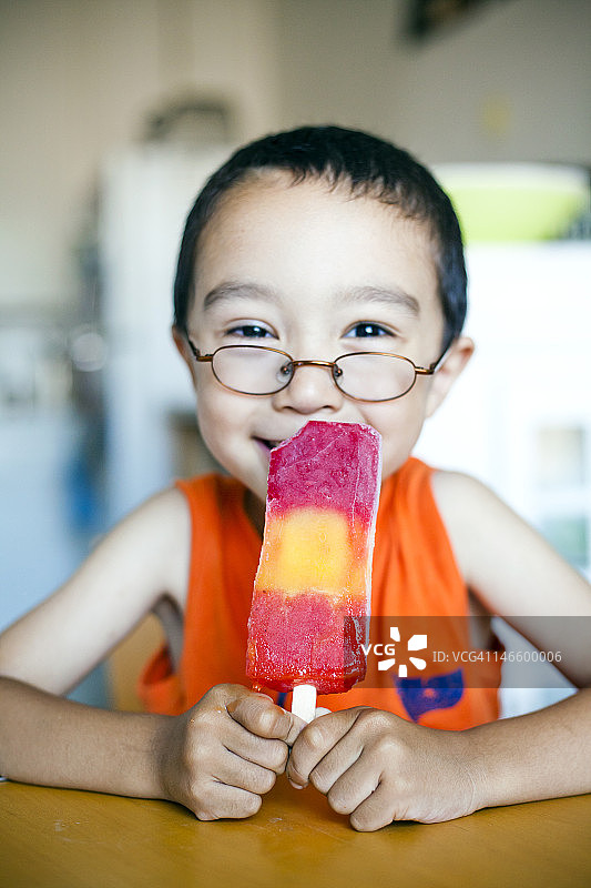 一个小男孩在厨房里吃冰棒。图片素材