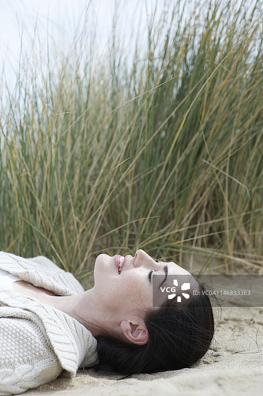 一个闭着眼睛躺在海滩上的女人。图片素材