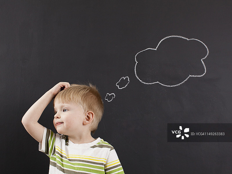 可爱的蹒跚学步的男孩(2-3)用粉笔写在黑板上的思想泡泡抓着他的头图片素材