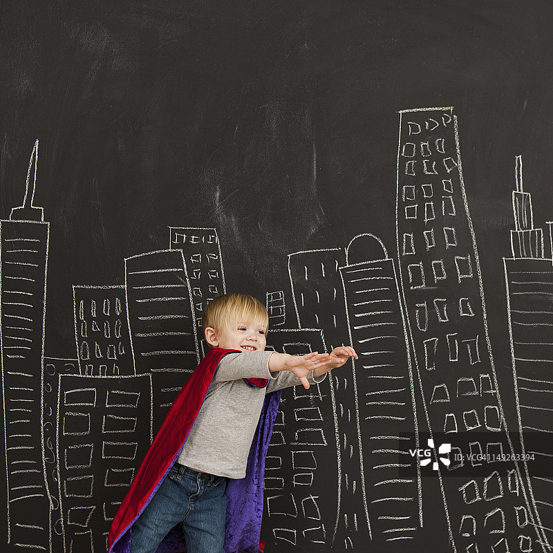 可爱的小男孩(2-3)站在黑板前，黑板上画着城市的轮廓线图片素材